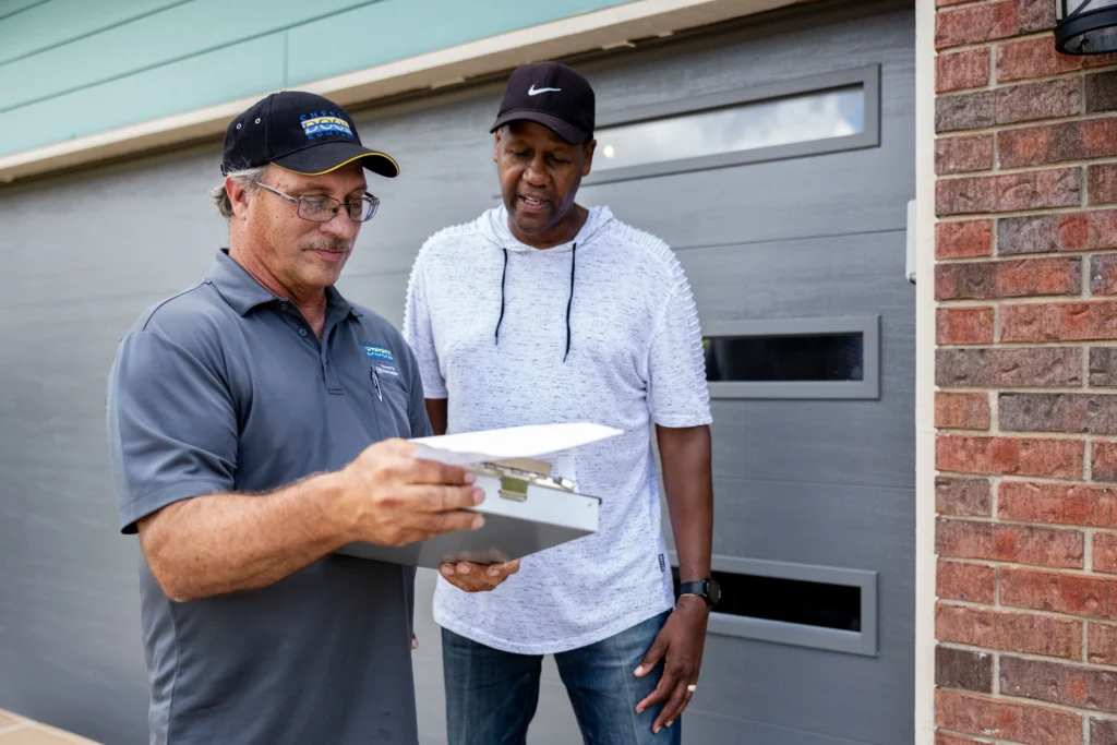 A garage-door technician reviewing paperwork with a customer outside their garage.